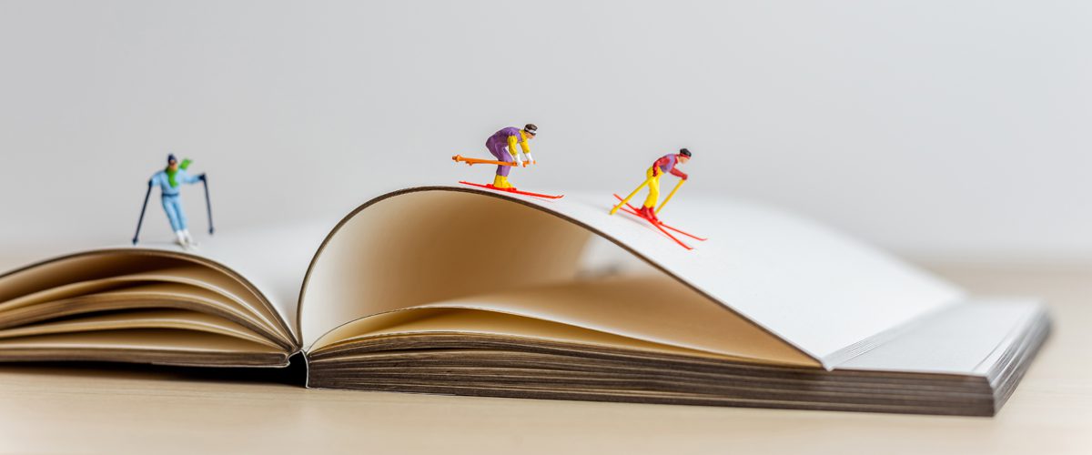 Miniature skiers sliding down the open book. Sport and travel concept.